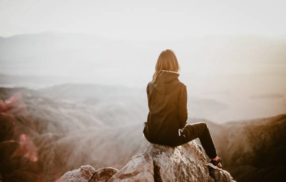 Frau sitzt auf einem Stein mit Panoramablick über die Berge